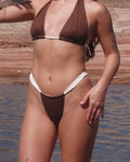 Person wearing a brown and white bikini standing by a body of water with rock formations.